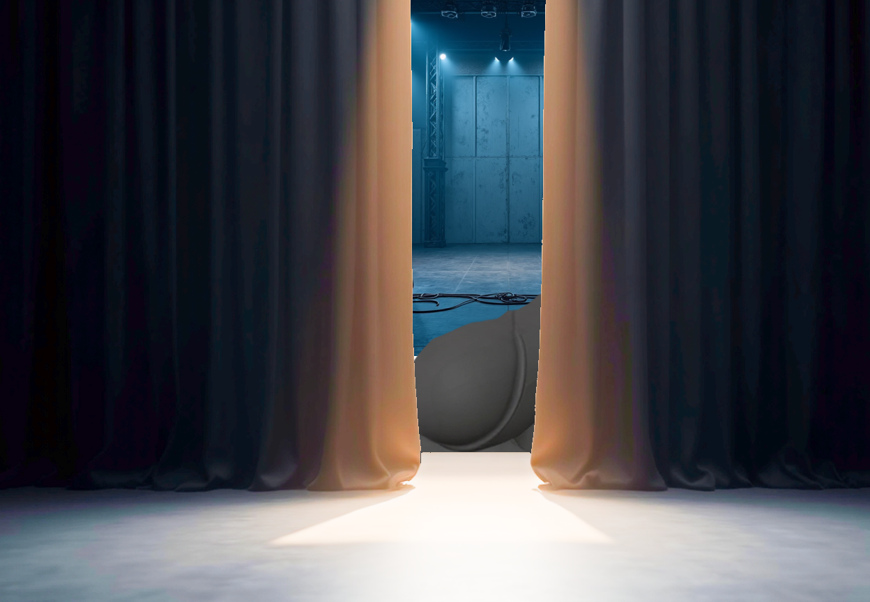 A dimly lit view from an audience, looking toward a stage where a thick black curtain is slightly open, revealing part of a large mechanical ride in spotlight and haze.